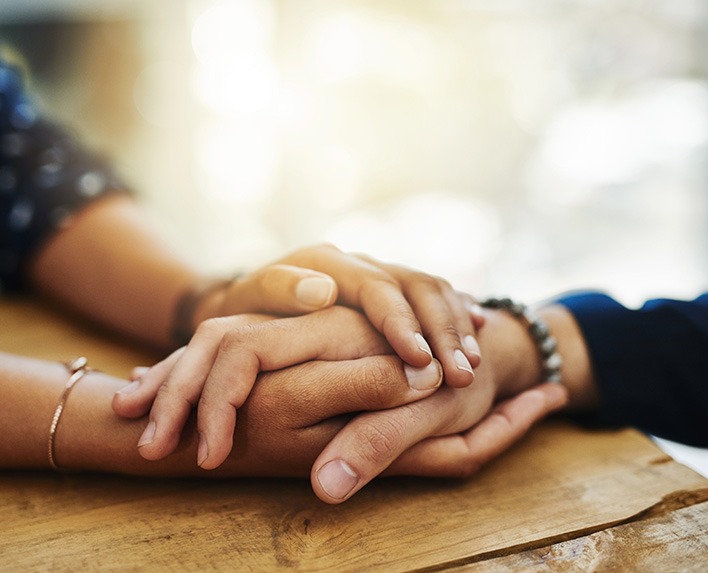 Uplifted Grief - two sets of hands intertwined on top of table